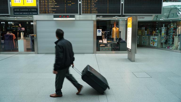 Ein Mann mit Koffer geht durch die Halle eines Flughafens.