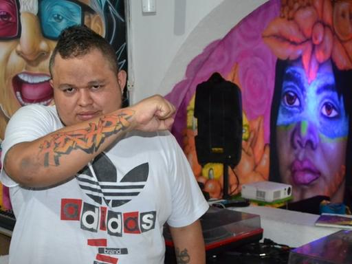 Der Künstler Jeihhco steht in einem Raum mit Graffiti vor zwei Schallplattenspielern