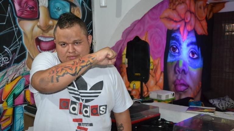Der Künstler Jeihhco steht in einem Raum mit Graffiti vor zwei Schallplattenspielern Der Künstler Jeihhco steht in einem Raum mit Graffiti vor zwei Schallplattenspielern