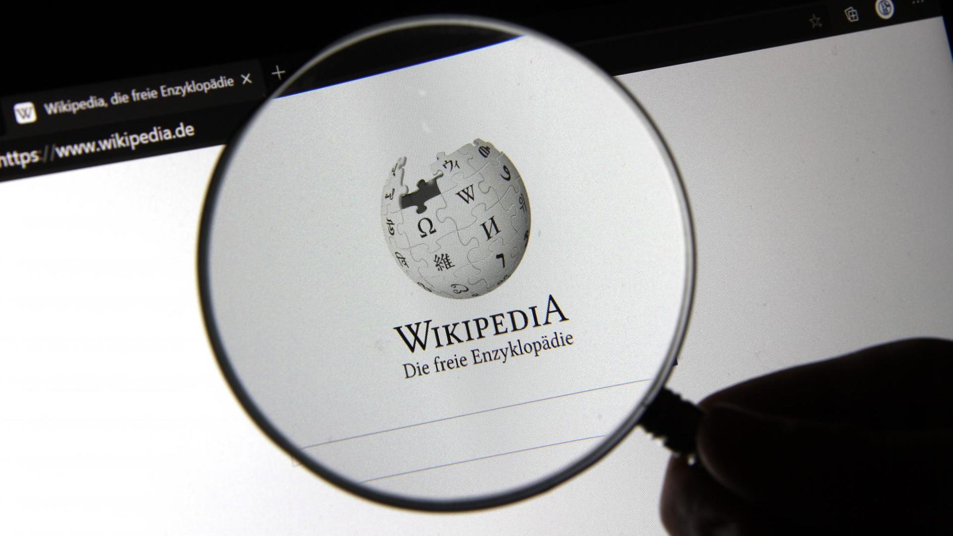 Durch eine Lupe ist das Logo der Online-Enzyklopädie Wikipedia zu sehen. 