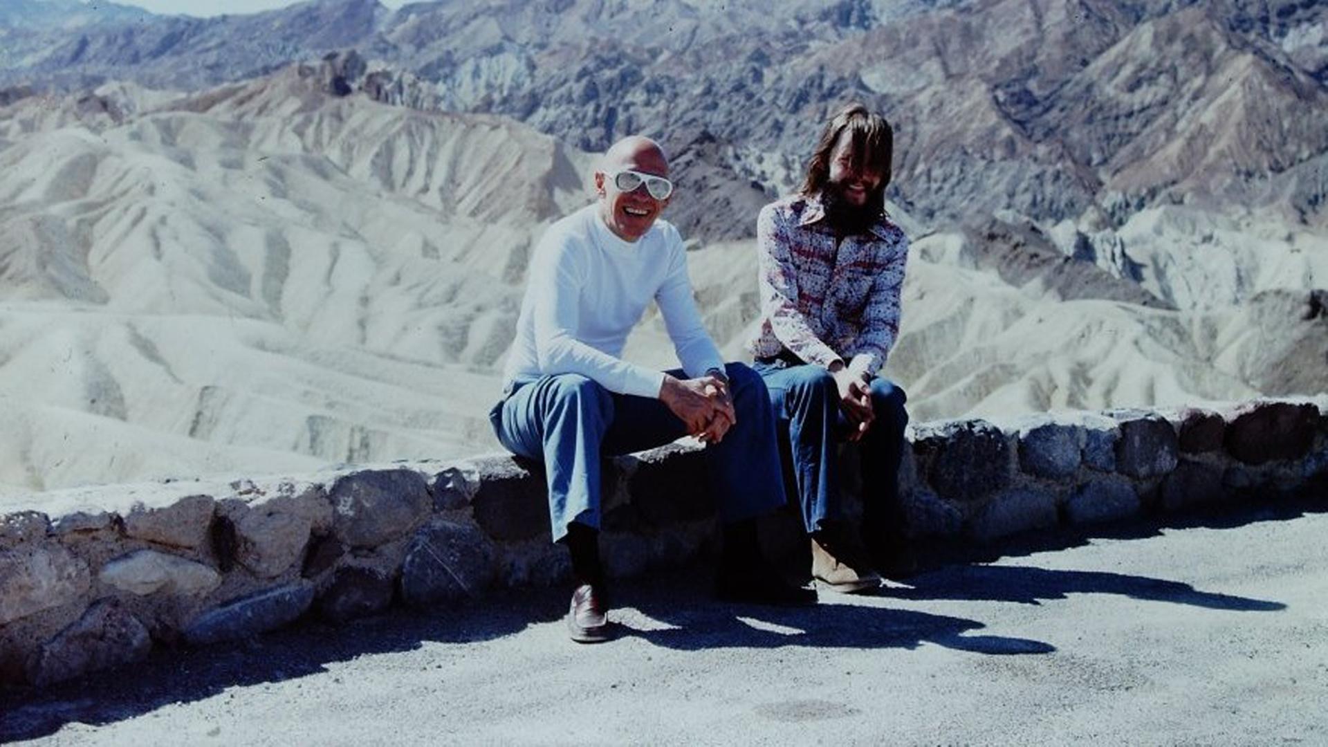 Am Rande einer Strasse auf einem kleinen Mäuerchen sitzen Foucault und Stoneman. Im Hintergrund die Berge vom Death Valley. Am Rande einer Strasse auf einem kleinen Mäuerchen sitzen Foucault und Stoneman. Im Hintergrund die Berge vom Death Valley.
