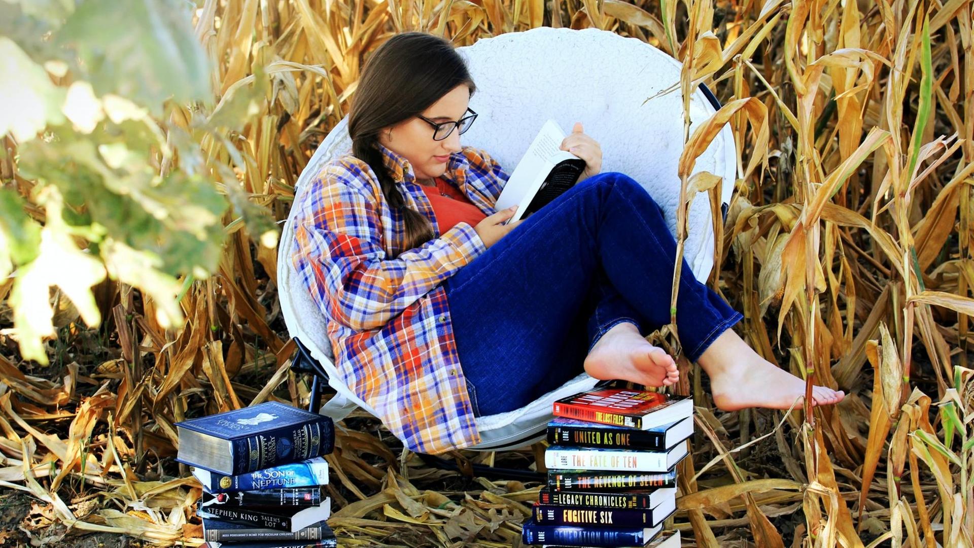 Eine Frau sitzt mit Büchern in einem Stuhl in einem Feld.