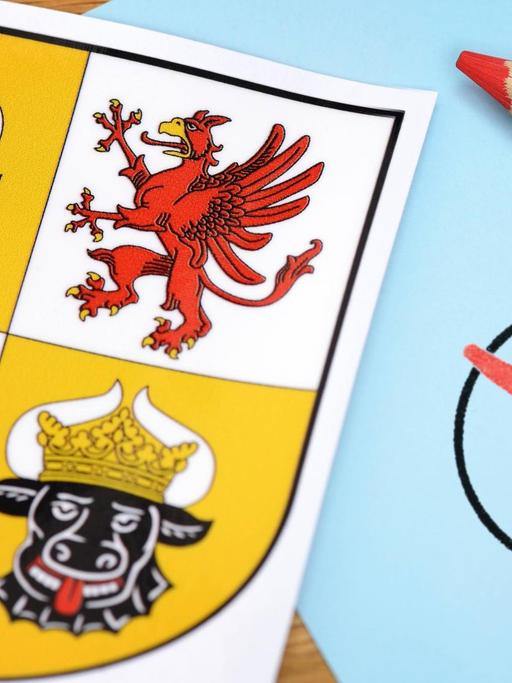 Landeswappen von Mecklenburg Vorpommern. Daneben liegt ein roter Stift, welcher ein Kreuz in einen Kreis zeichnet.