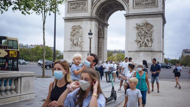 Paris: Touristen mit Schutzmasken spazieren auf der Prachtstraße Champs-Elysees, im Hintergrund steht der Arc de Triomphe.