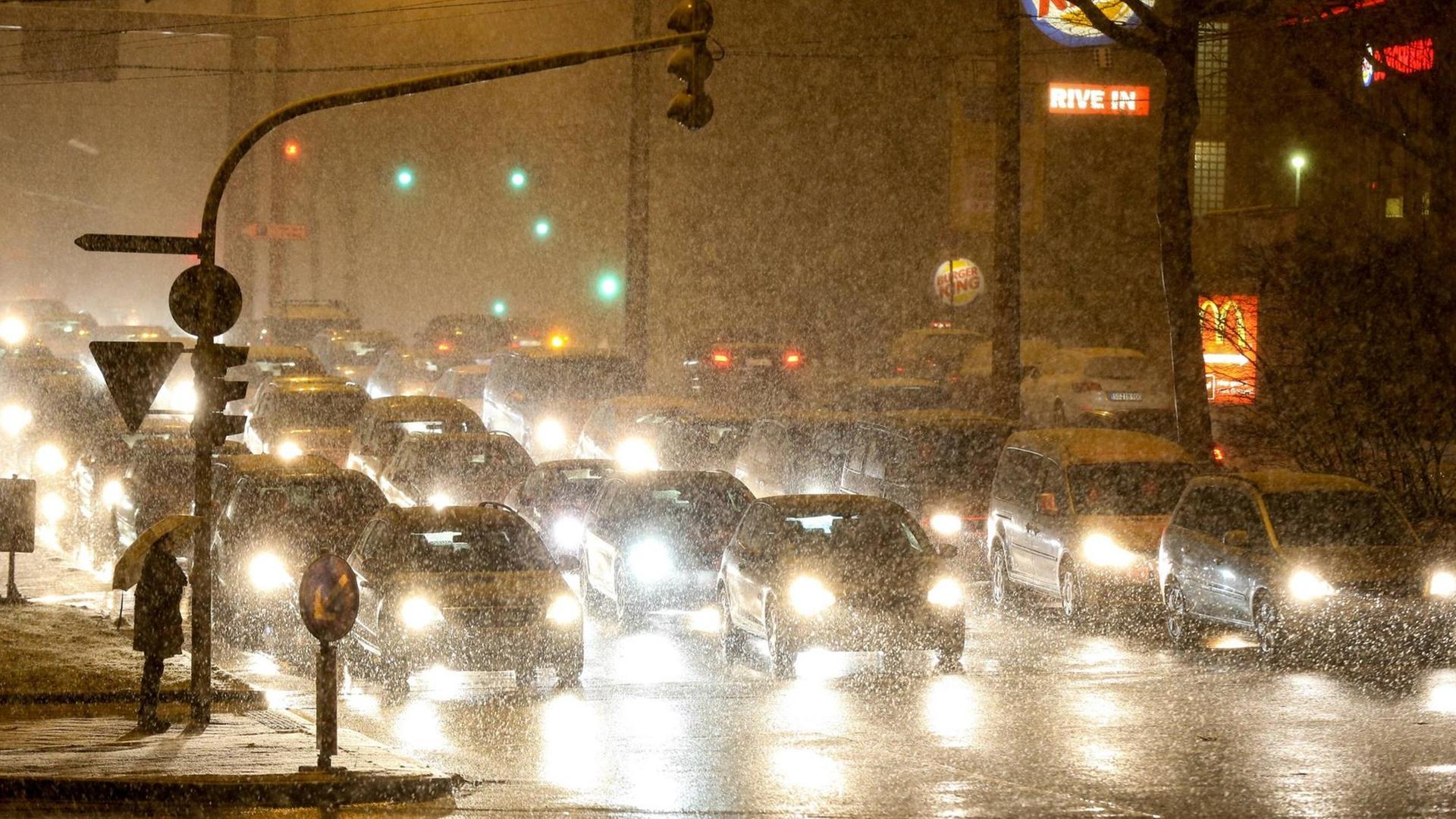 Autos fahren am Abend auf einer regennassen Straße in einer Stadt.