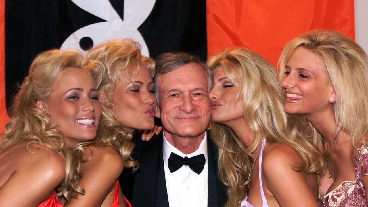 Das Bild zeigt Hugh Hefner, den Gründer des "Playboy" im Jahr 1999 in Cannes. Er wird von mehreren blonden Frauen geküsst.
