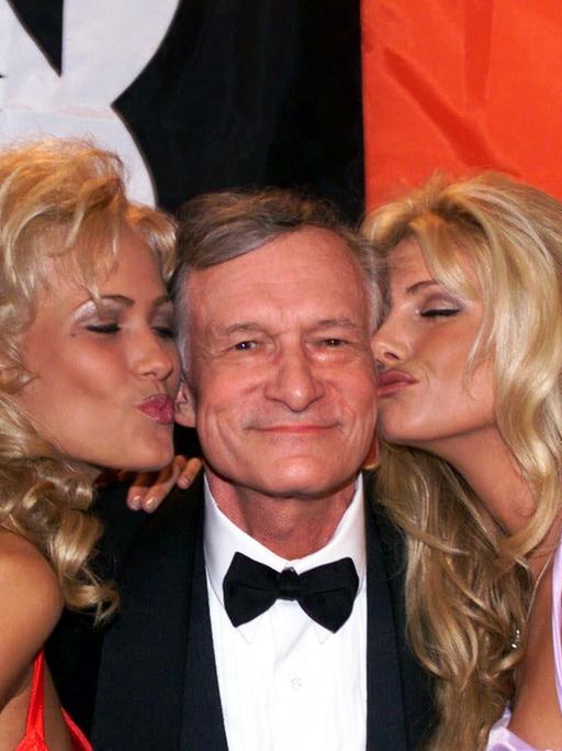 Das Bild zeigt Hugh Hefner, den Gründer des "Playboy" im Jahr 1999 in Cannes. Er wird von mehreren blonden Frauen geküsst.
