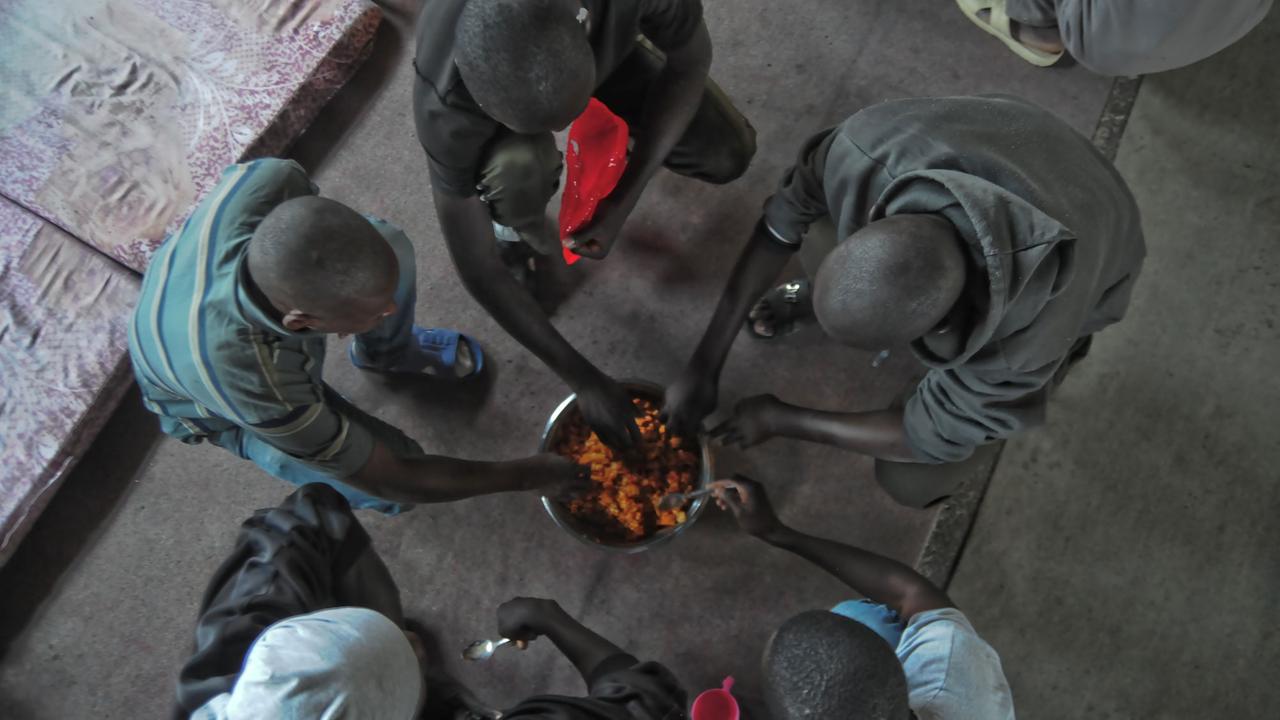 Afrikanische Geflüchtete knien am 5.04.2017 in einem Flüchtlingslager in Tripolis (Libyen) um eine Schale mit Essen. Afrikanische Geflüchtete knien am 5.04.2017 in einem Flüchtlingslager in Tripolis (Libyen) um eine Schale mit Essen.