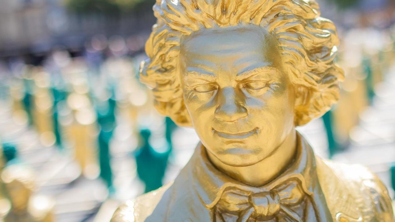 Nahaufnahme eines goldenen, lächelnden Beethoven-Gesichtes, das während der Installation im Mai 2019 in Bonn entstand, bei der 700 lächelnde Figuren den zentralen Platz in Bonn füllten. Nahaufnahme eines goldenen, lächelnden Beethoven-Gesichtes, das während der Installation im Mai 2019 in Bonn entstand, bei der 700 lächelnde Figuren den zentralen Platz in Bonn füllten.