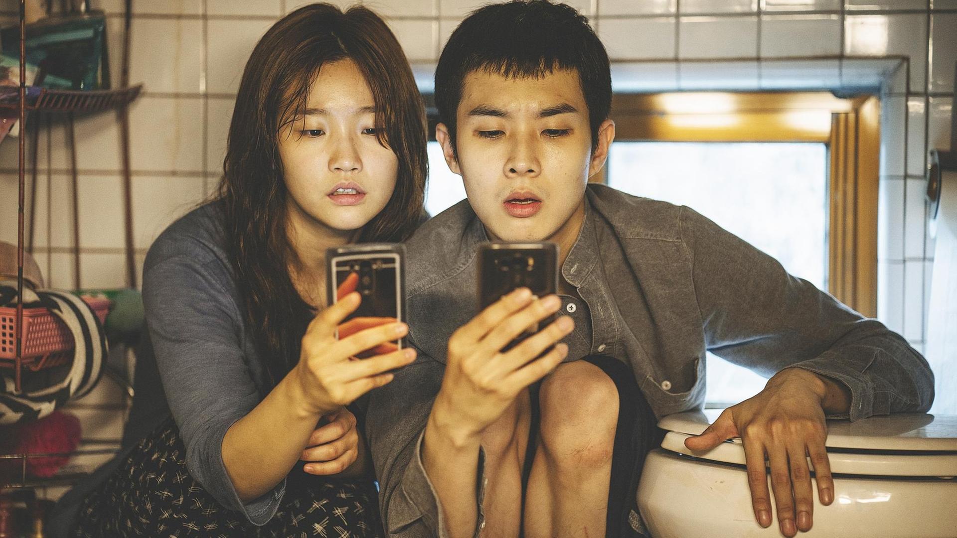 Die Darsteller Park So-dam und Choi Woo-shik in Bong Joon-hos Spielfilm "Parasite" starren auf Smartphones