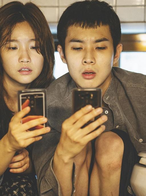 Die Darsteller Park So-dam und Choi Woo-shik in Bong Joon-hos Spielfilm "Parasite" starren auf Smartphones
