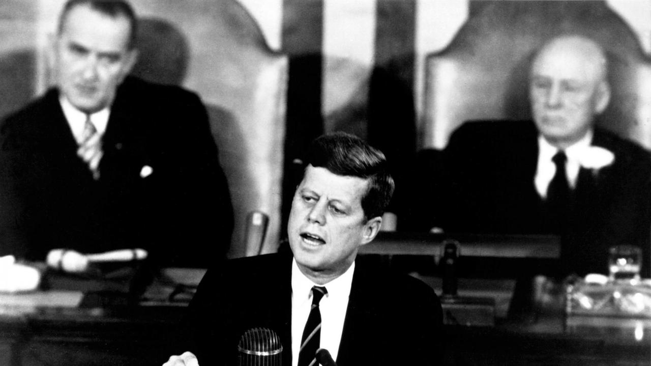 Der amerikanische Präsident John F. Kennedy hält am 25. Mai 1961vor dem Kongress in Washington D.C. seine berühmt gewordene Rede zur bemannten Raumfahrt: "I believe this nation should commit itself to achieving the goal, before this decade is out, of landing a man on the Moon and returning him safely to the Earth". Hinten links Vizepräsident Lyndon B. Johnson, rechts Senatssprecher Sam T. Rayburn. Kennedy beschrieb in seiner Rede die Vision einer bemannten Mondlandung noch vor Ende der Dekade Der amerikanische Präsident John F. Kennedy hält am 25. Mai 1961vor dem Kongress in Washington D.C. seine berühmt gewordene Rede zur bemannten Raumfahrt: "I believe this nation should commit itself to achieving the goal, before this decade is out, of landing a man on the Moon and returning him safely to the Earth". Hinten links Vizepräsident Lyndon B. Johnson, rechts Senatssprecher Sam T. Rayburn. Kennedy beschrieb in seiner Rede die Vision einer bemannten Mondlandung noch vor Ende der Dekade