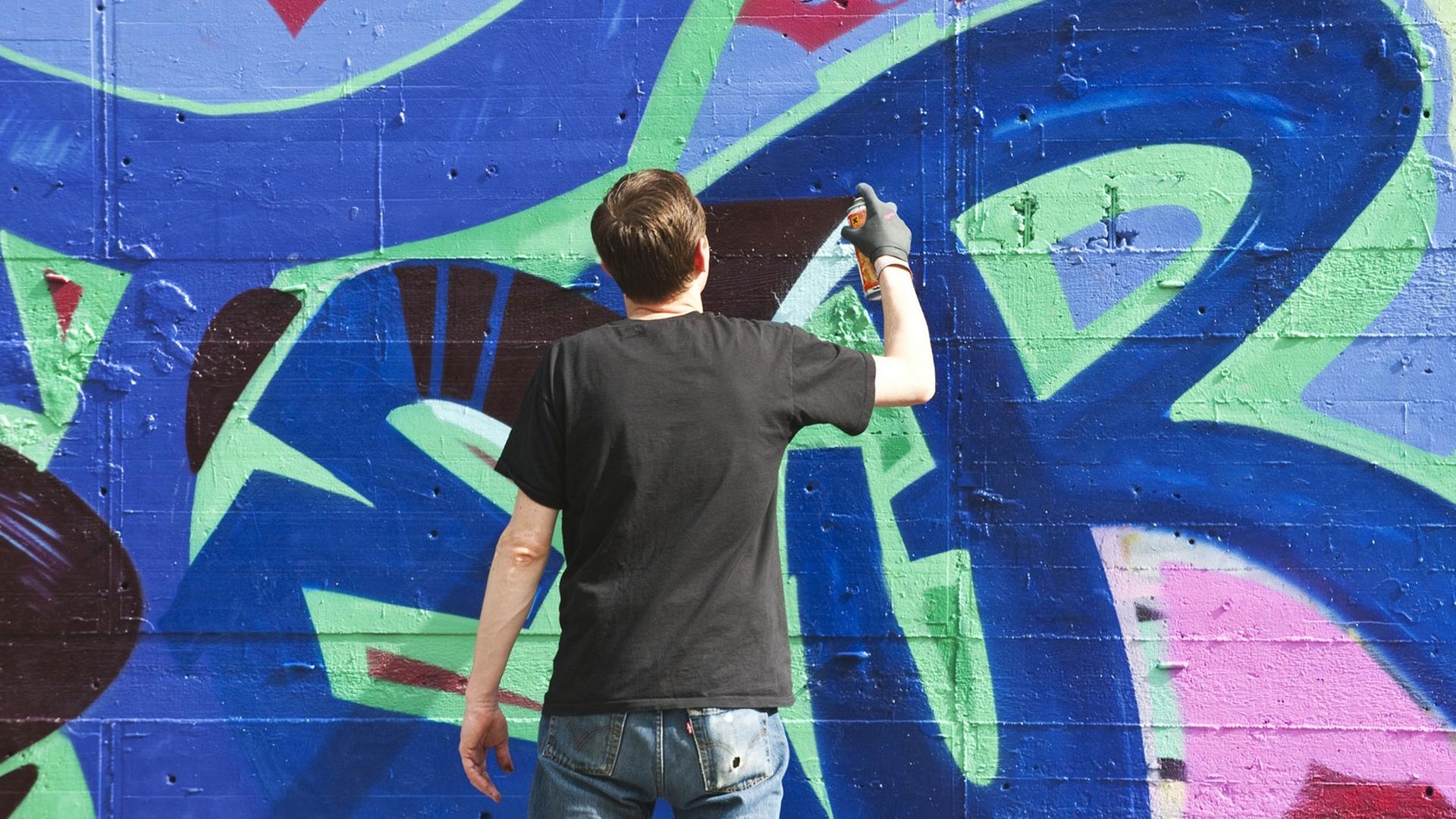 Ein Sprayer schreibt einen Schriftzug an eine Wand Ein Sprayer schreibt einen Schriftzug an eine Wand