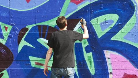 Ein Sprayer schreibt einen Schriftzug an eine Wand