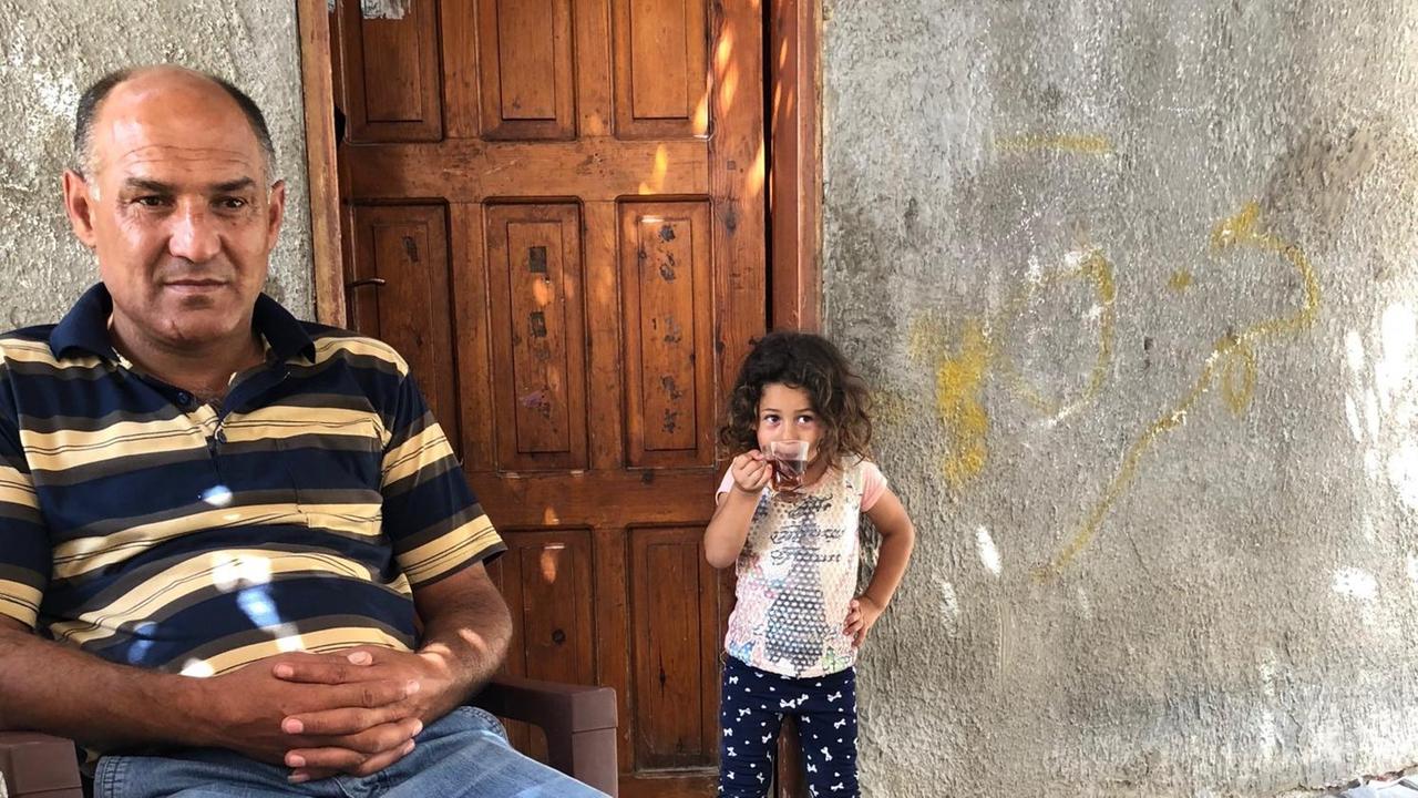 Raed Atamneh, Fahrer für Gäste im Gazastreifen, sitzt vor einer Tür im Hintergrund ein kleines Mädchen, das in die Kamera schaut Raed Atamneh, Fahrer für Gäste im Gazastreifen, sitzt vor einer Tür im Hintergrund ein kleines Mädchen, das in die Kamera schaut