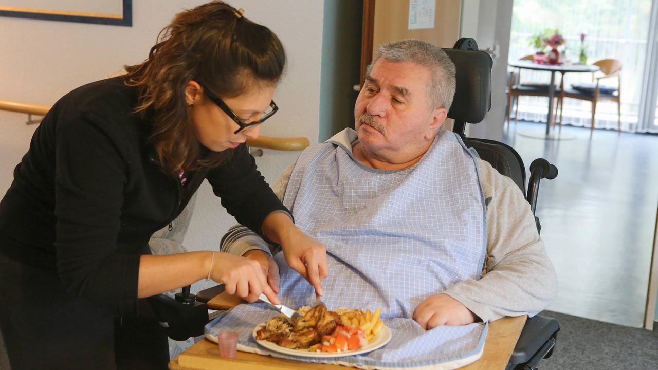 Eine Mitarbeiterin schneidet einem Pflegebedürftigen das Essen zurecht - hier im Multikulturellen Seniorenzentrum des Deutschen Roten Kreuzes, Haus am Sandberg, in Duisburg Eine Mitarbeiterin schneidet einem Pflegebedürftigen das Essen zurecht - hier im Multikulturellen Seniorenzentrum des Deutschen Roten Kreuzes, Haus am Sandberg, in Duisburg