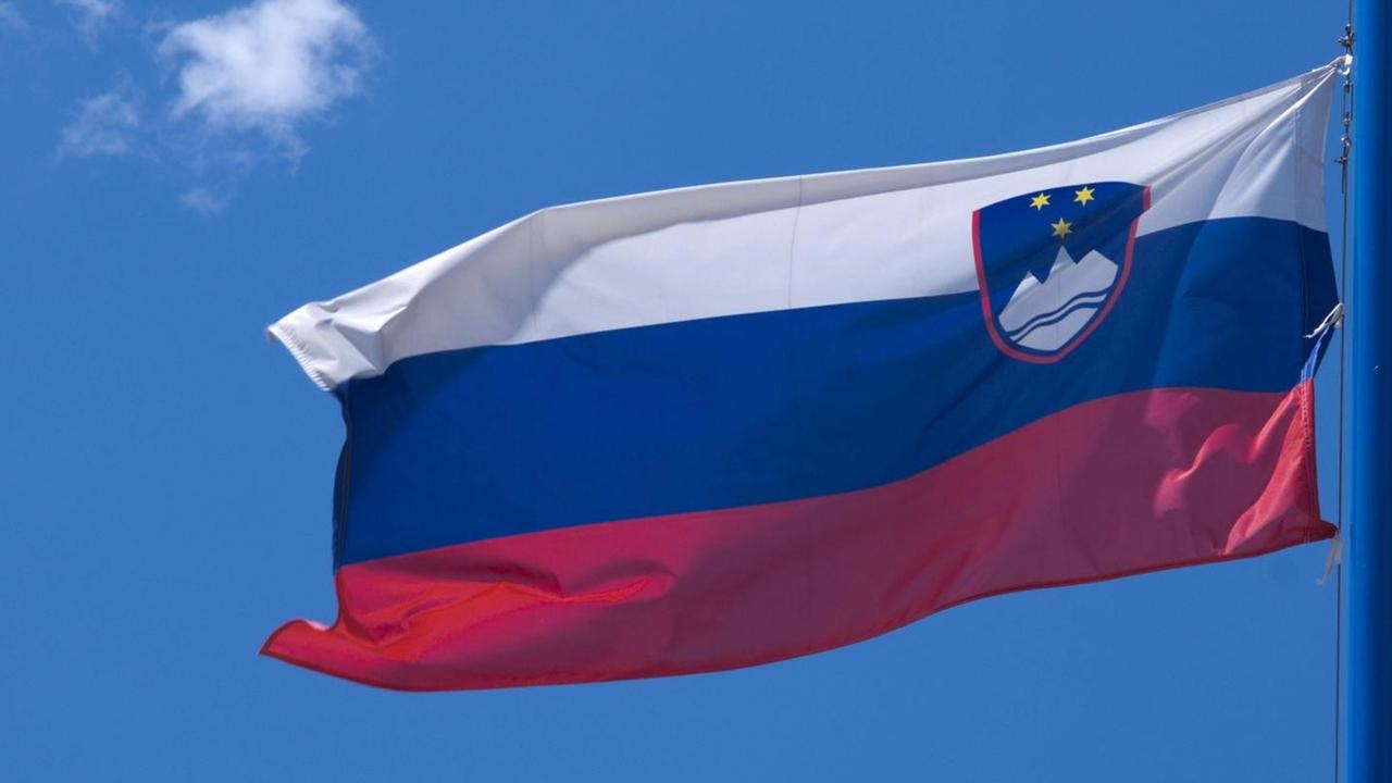 Die Flagge von Slowenien, im Hintergrund blauer Himmel und ein weiße Wolke