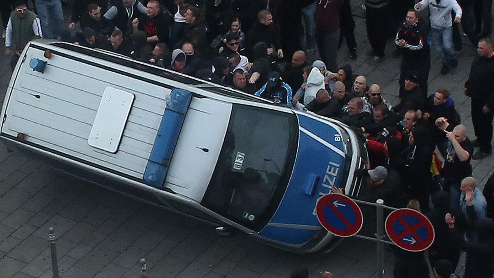Bei einer Demonstration der Gruppe "Hooligans gegen Salafismus" in Köln wird ein Polizeiauto umgeworfen.