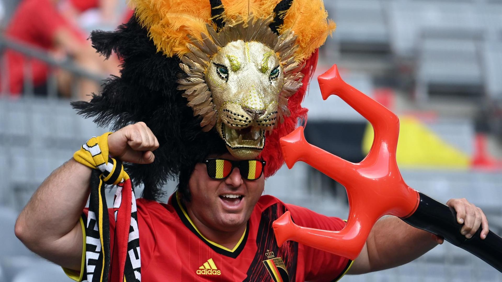 Ein Fan bei der Fußball-EM mit Sonnenbrille in belgischen Landesfarben, Löwenkopfschmuck und Aufblas-Dreizack. Ein Fan bei der Fußball-EM mit Sonnenbrille in belgischen Landesfarben, Löwenkopfschmuck und Aufblas-Dreizack.