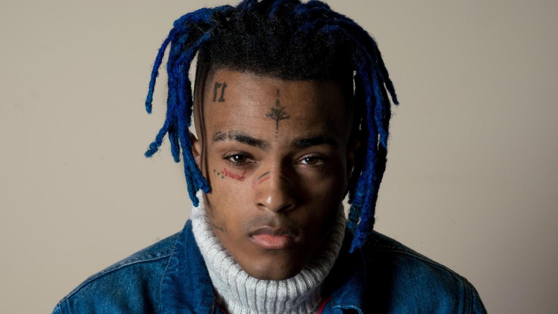 Der Rapper XXXTentacion mit blauen Rastazöpfen und Tattoos im Gesicht blickt in die Kamera