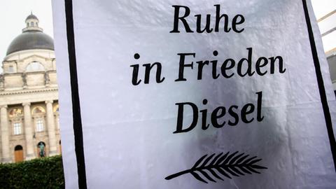 Eine Greenpeace-Aktivistin trägt während des Diesel-Gipfels hinter der Staatskanzlei in München (Bayern) ein Banner mit der Aufschrift "Ruhe in Frieden Diesel".