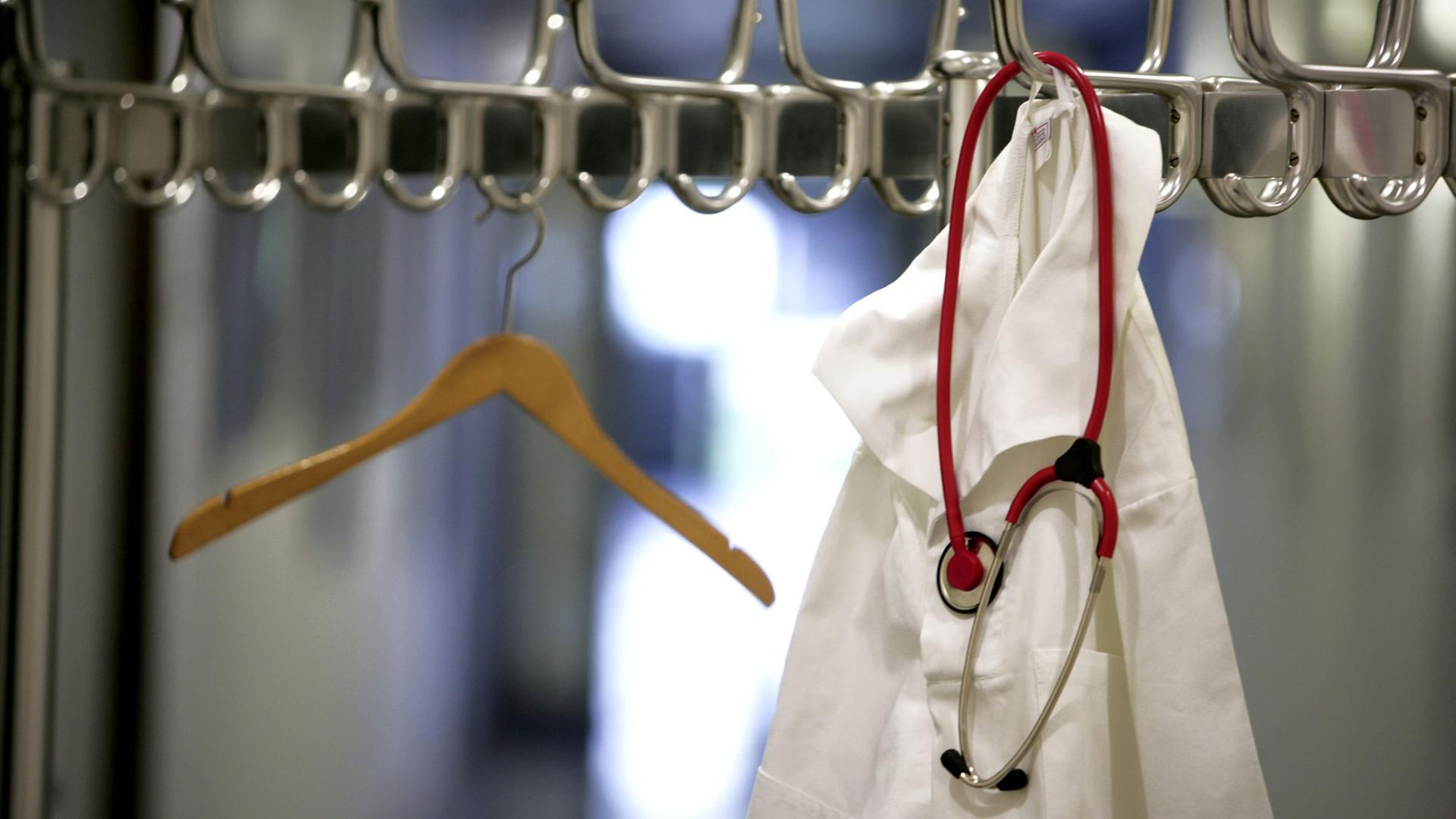 Ein Arztkittel und Stethoskop hängt an einer Garderobenständer.