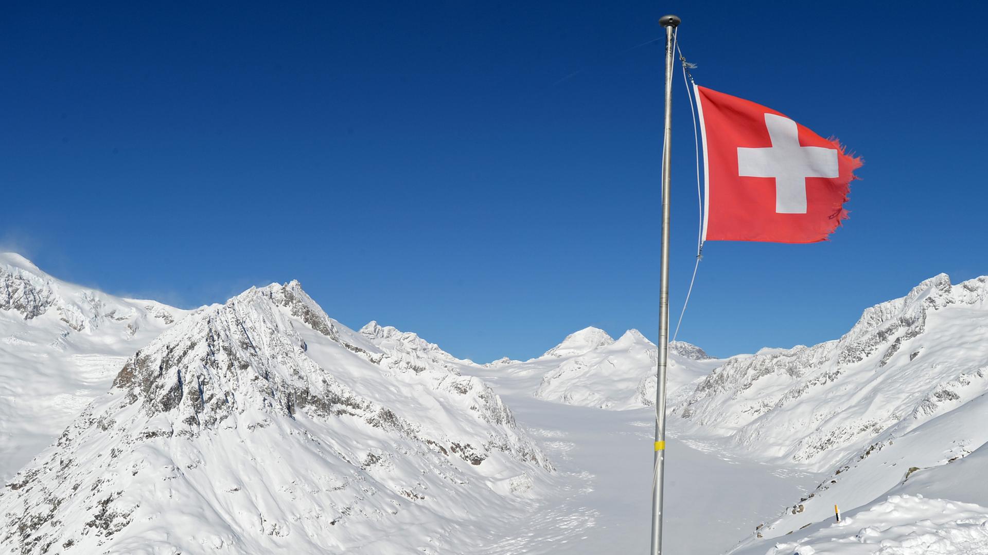 Die Schweizer Nationalfahne weht bei strahlendem Sonnenschein nahe dem Eggishorn bei Fiesch (Wallis) in der Schweiz.