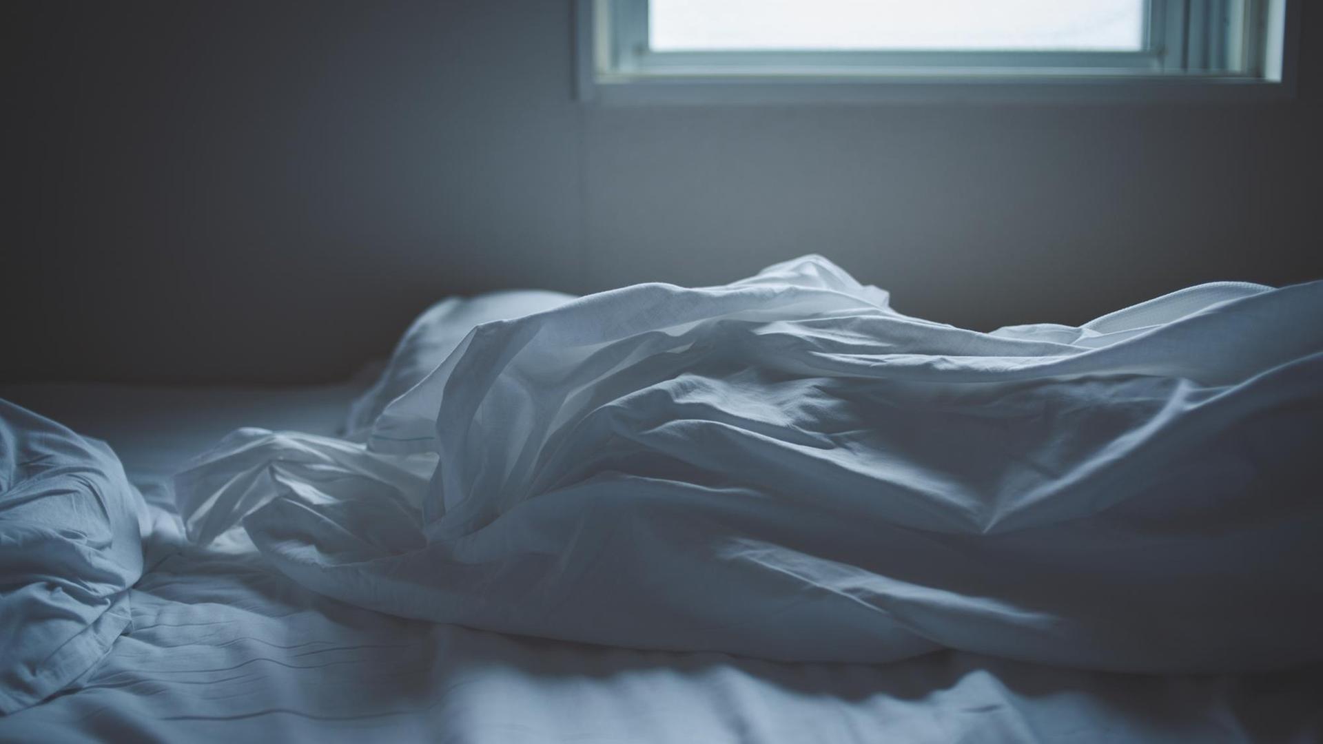 Ein unordentliches Bett mit weißen Laken. Durch das Fenster im Hintergrund fällt Licht aufs Bett. Ein unordentliches Bett mit weißen Laken. Durch das Fenster im Hintergrund fällt Licht aufs Bett.