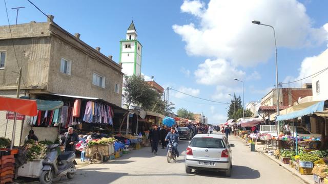 Eine Straße in einer Vorstadt von Tunis mit Obst-Geschäften, Autos und Menschen.