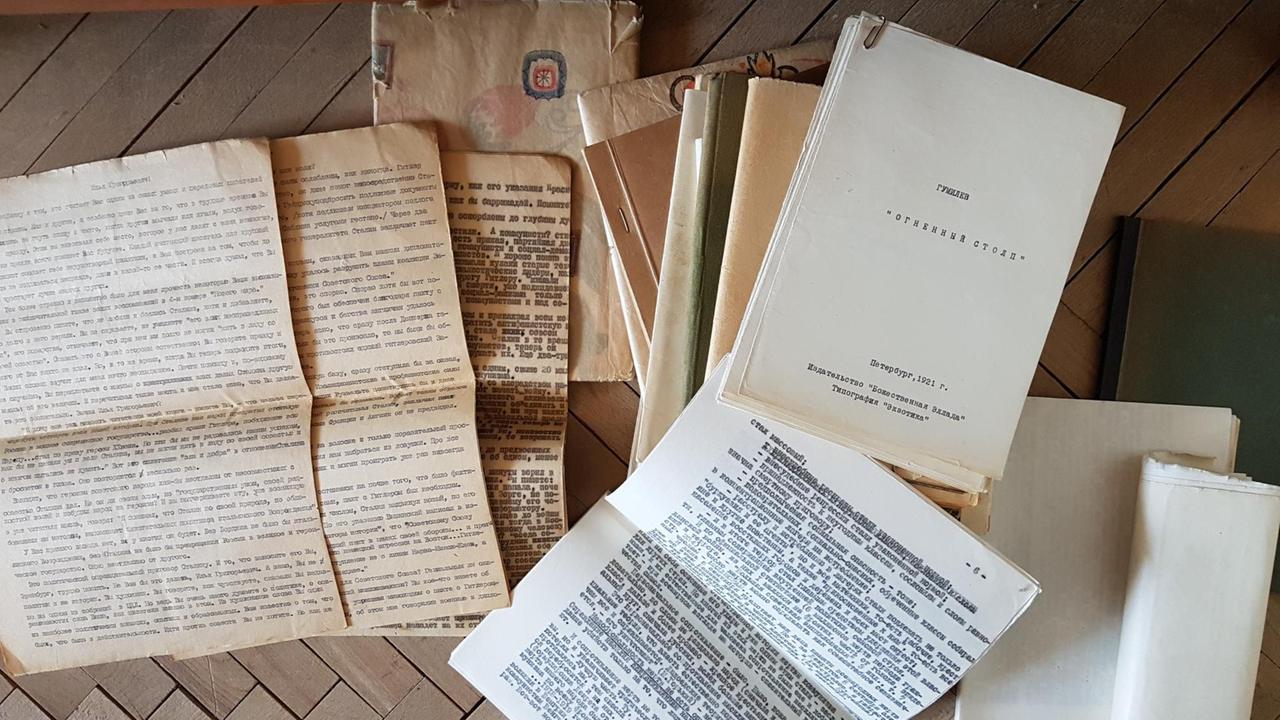 Vergilbte, mit Schreibmaschine verfasste Schriftdokumente und selbstgeheftete Bücher liegen auf einem Holzboden.