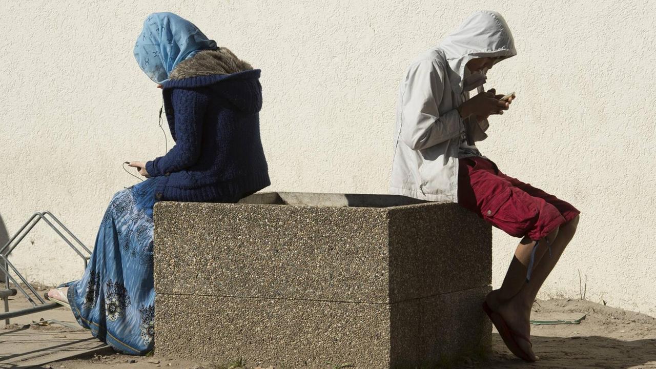 Heidelberg, DEU, 29.09.2015: Die ehemalige US-Kaserne Patrick-Henry-Village ist zu einem Drehkreuz fuer die Erstaufnahme von Fluechtlingen im Suedwesten geworden. Hier wird die erkennungsdienstliche Behandlung sowie den Gesundheitscheck erledigt. Hinterher werden die Asylbewerber entweder direkt in die Kommunen oder in andere Erstaufnahmeeinrichtungen verteilt werden. Eine junge Frau und ein junger Mann sitzen gebaeugt auf ihre Smartphones. Heidelberg DEU 29 09 2015 the former U.S. Barracks Patrick Henry Village is to a Hub for the Initial recording from Refugees in Southwest become here will the erkennungsdienstliche Treatment and the Health Check done behind will the Asylum-seekers Either directly in the Municipalities Or in other distributed will a Boy Woman and a young Man sit on theirs Smartphones Heidelberg, DEU, 29.09.2015: Die ehemalige US-Kaserne Patrick-Henry-Village ist zu einem Drehkreuz fuer die Erstaufnahme von Fluechtlingen im Suedwesten geworden. Hier wird die erkennungsdienstliche Behandlung sowie den Gesundheitscheck erledigt. Hinterher werden die Asylbewerber entweder direkt in die Kommunen oder in andere Erstaufnahmeeinrichtungen verteilt werden. Eine junge Frau und ein junger Mann sitzen gebaeugt auf ihre Smartphones. Heidelberg DEU 29 09 2015 the former U.S. Barracks Patrick Henry Village is to a Hub for the Initial recording from Refugees in Southwest become here will the erkennungsdienstliche Treatment and the Health Check done behind will the Asylum-seekers Either directly in the Municipalities Or in other distributed will a Boy Woman and a young Man sit on theirs Smartphones