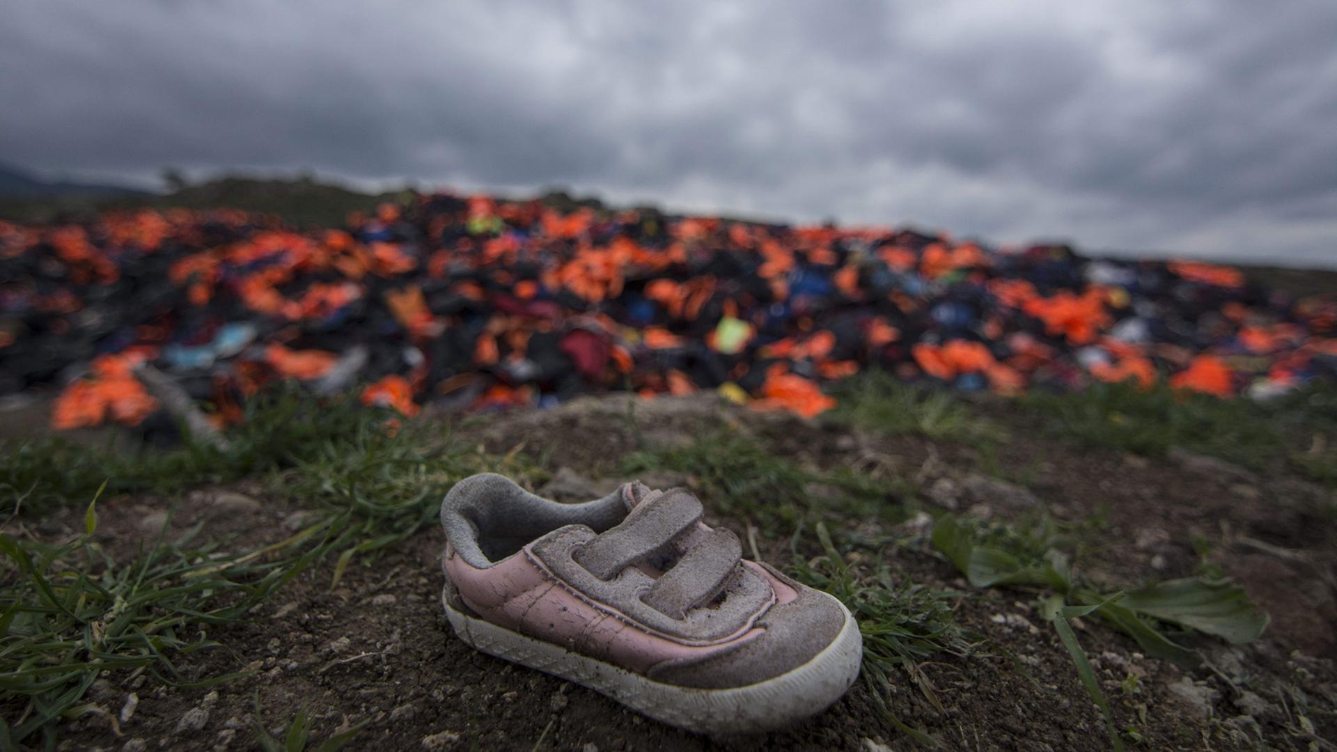 Tausende von Schwimmwesten, die von Flüchtlingen genutzt wurden, stapeln sich auf einer Wiese auf Lesbos. Im Vordergrund ein schmutzig-rosa Kinderschuh. Tausende von Schwimmwesten, die von Flüchtlingen genutzt wurden, stapeln sich auf einer Wiese auf Lesbos. Im Vordergrund ein schmutzig-rosa Kinderschuh.