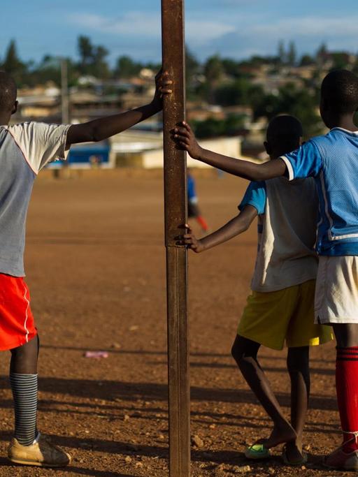 Mehrere Kinder stehen während eines Fußballspiels an den Torpfosten gelehnt.