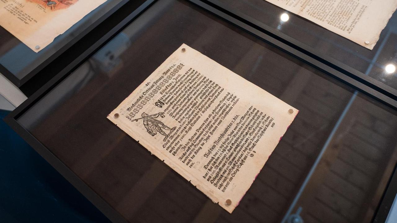 Einzelne Seiten historischer Zeitungen liegen in einer Glasvitrine. Einzelne Seiten historischer Zeitungen liegen in einer Glasvitrine.