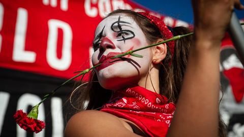 Eine junge Frau mit bemalten Gesicht und einer roten Nelke zwischen den Zähnen demonstriert in Santiago de Chile gegen Polizeigewalt.