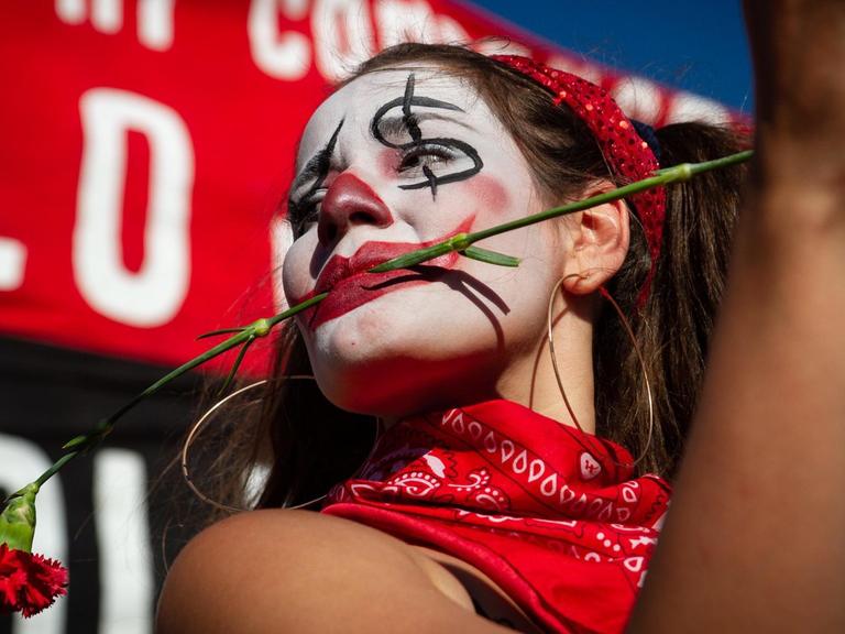 Eine junge Frau mit bemalten Gesicht und einer roten Nelke zwischen den Zähnen demonstriert in Santiago de Chile gegen Polizeigewalt.
