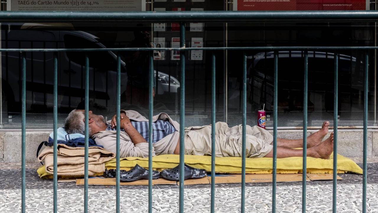 Ein obdachloser Mann schläft in einer Fußgängerzone vor einer Bank