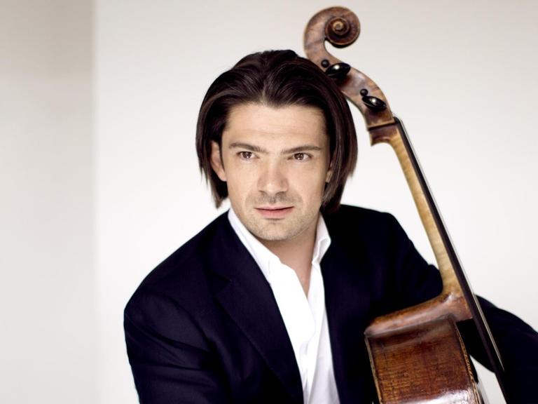 Der Cellist Gautier Capuçon sitzend, er umarmt sein Instrument, hält in der rechten Hand den Bogen. Er trägt einen schwarzen Anzug und ein weißes Hemd