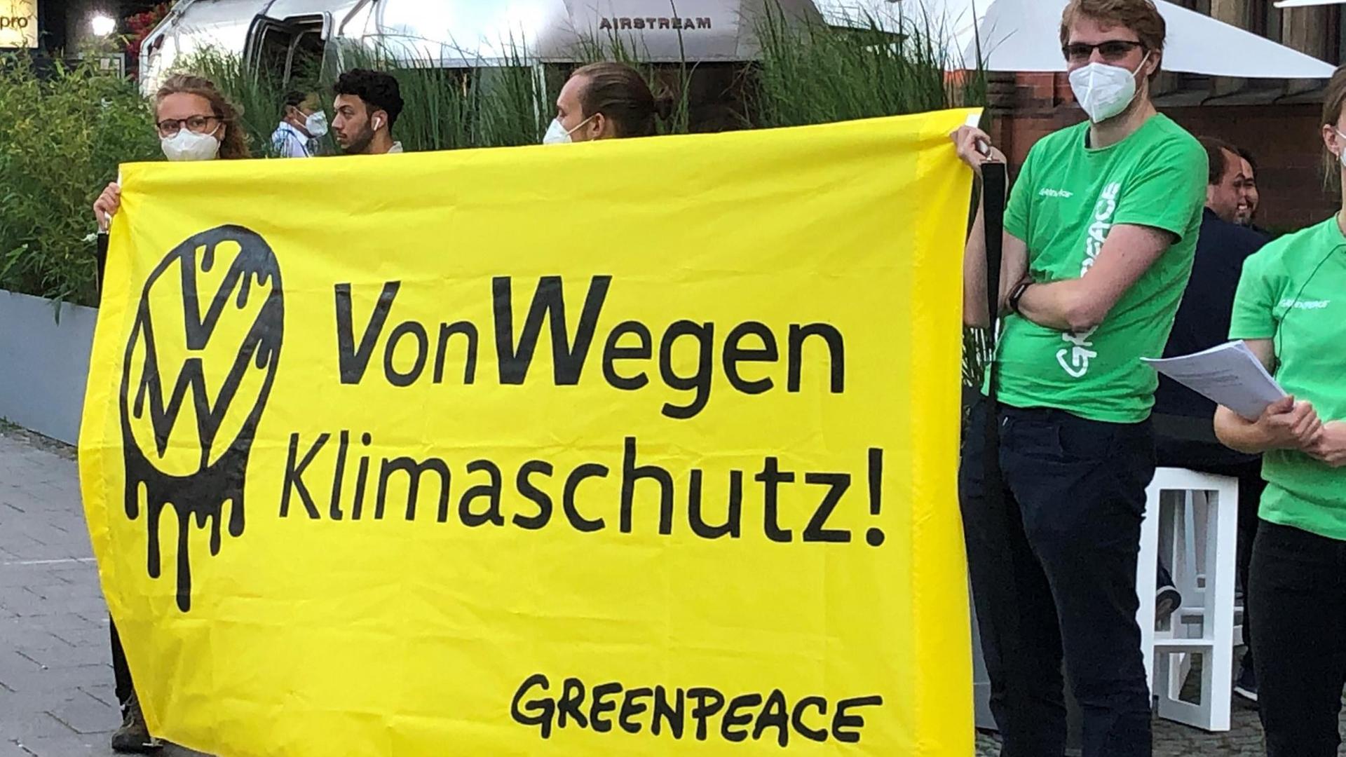Demonstranten von Greenpeace stehen mit einem Poster "VW - Von Wegen Klimaschutz!" vor einer Halle, in der eine Veranstaltung von Volkswagen stattfand. 