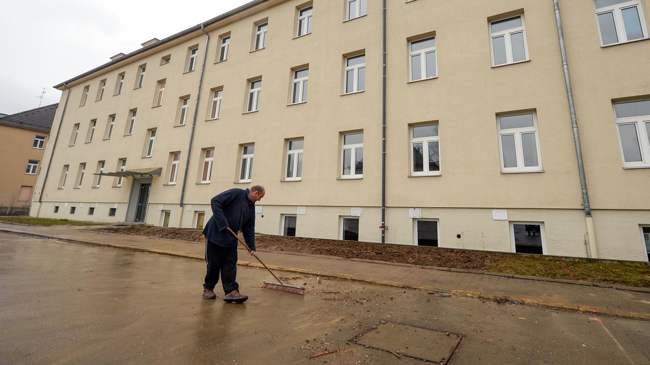 Ein Hausmeister fegt vor einem Gebäude. Ein Hausmeister fegt vor einem Gebäude.