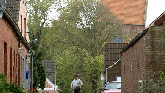 Ein Mann geht am Dienstag 16. Oktober 2007 über eine kleine Wohnstraße im Ort Suurhusen im Kreis Aurich. Im Hintergrund ist der mit einem Überhang von 2,43 Metern schiefste Kirchturm der Welt zu sehen, der es bis zu einem Eintrag ins Guinness-Buch der Rekorde schaffte.
