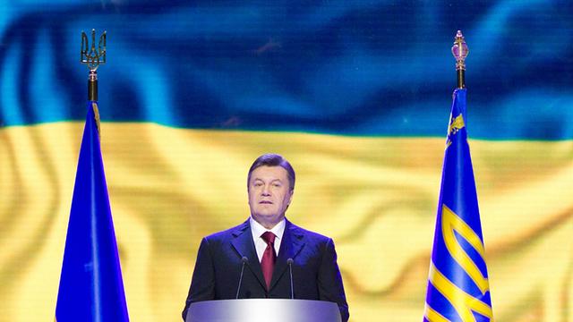Der ukrainischen Präsident Viktor Janukowitsch steht flankiert von zwei blau-gelben Fahnen an einem Rednerpult.