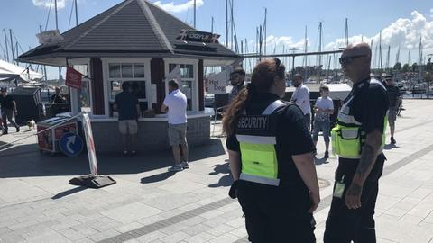 Zwei Mitarbeiter eines Sicherheitsdienstes stehen vor einem Imbiss in Heiligenhafen und kontrollieren, ob die Corona-Vorschriften eingehalten werden.