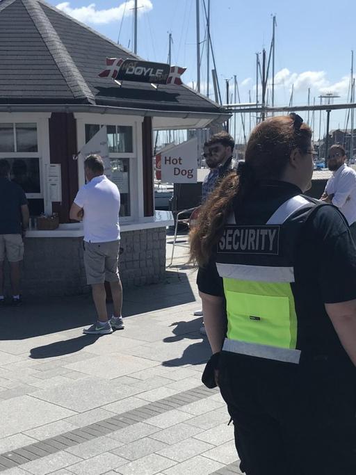 Zwei Mitarbeiter eines Sicherheitsdienstes stehen vor einem Imbiss in Heiligenhafen und kontrollieren, ob die Corona-Vorschriften eingehalten werden.