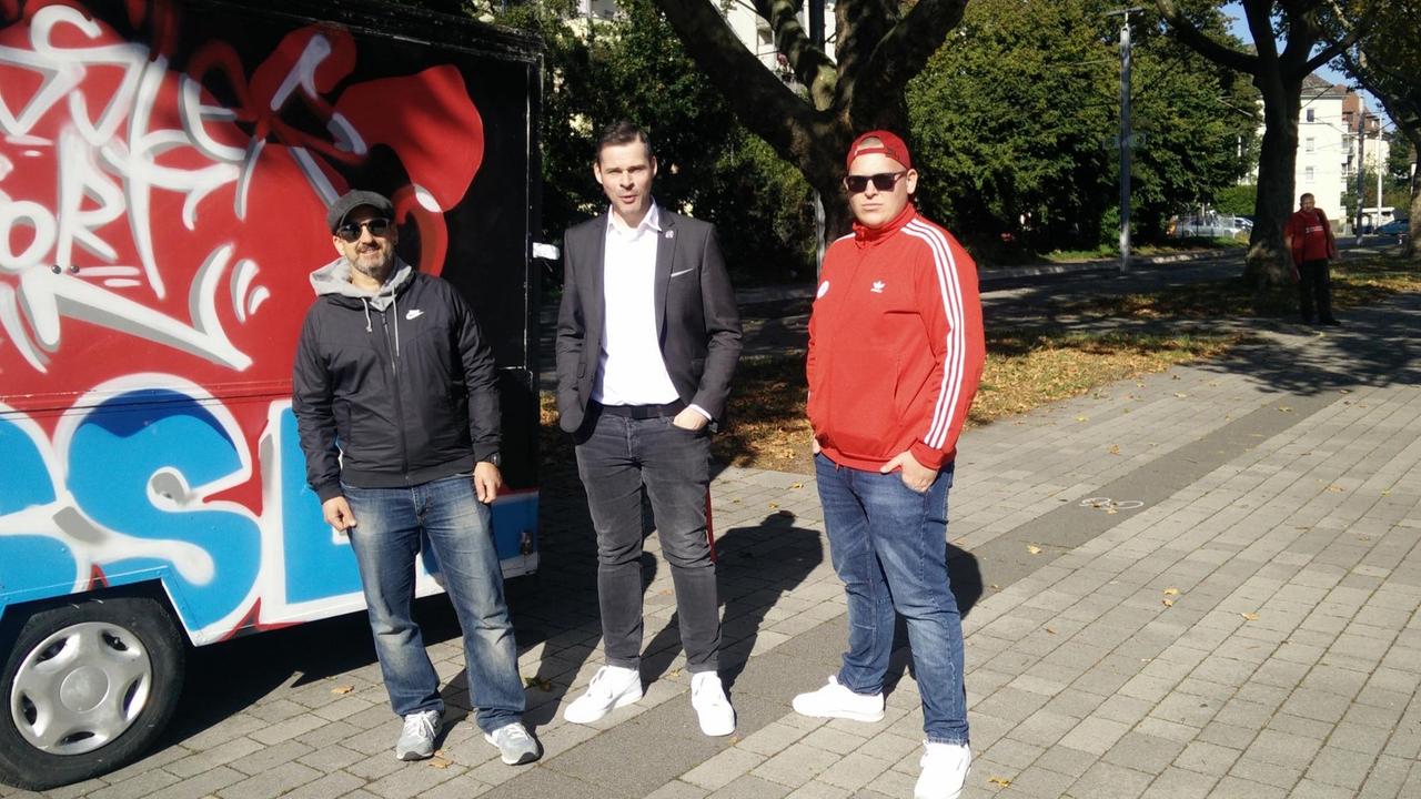 Neben mit einem Graffiti besprühten Bus stehen drei Männer. Neben mit einem Graffiti besprühten Bus stehen drei Männer.