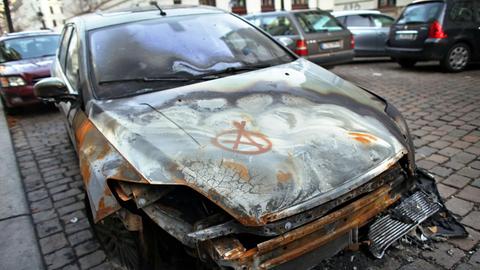 Das Wrack eines von einem Feuer zerstörten Autos steht am 03.12.2013 in Leipzig (Sachsen) in einer Nebenstraße. Darauf ist das Anarchie-Zeichen gesprüht.