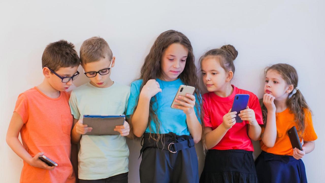 Schulmädchen und Schuljungen in bunten T-Shirts, schauen während der Pause auf ihre Smartphones. Schulmädchen und Schuljungen in bunten T-Shirts, schauen während der Pause auf ihre Smartphones.