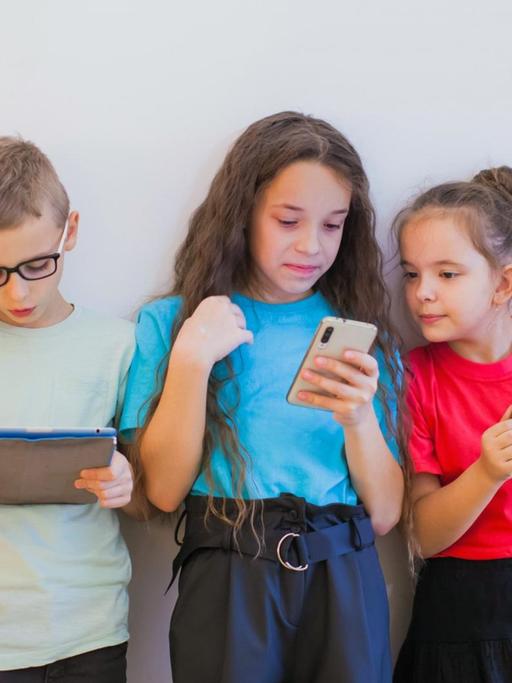 Schulmädchen und Schuljungen in bunten T-Shirts, schauen während der Pause auf ihre Smartphones.