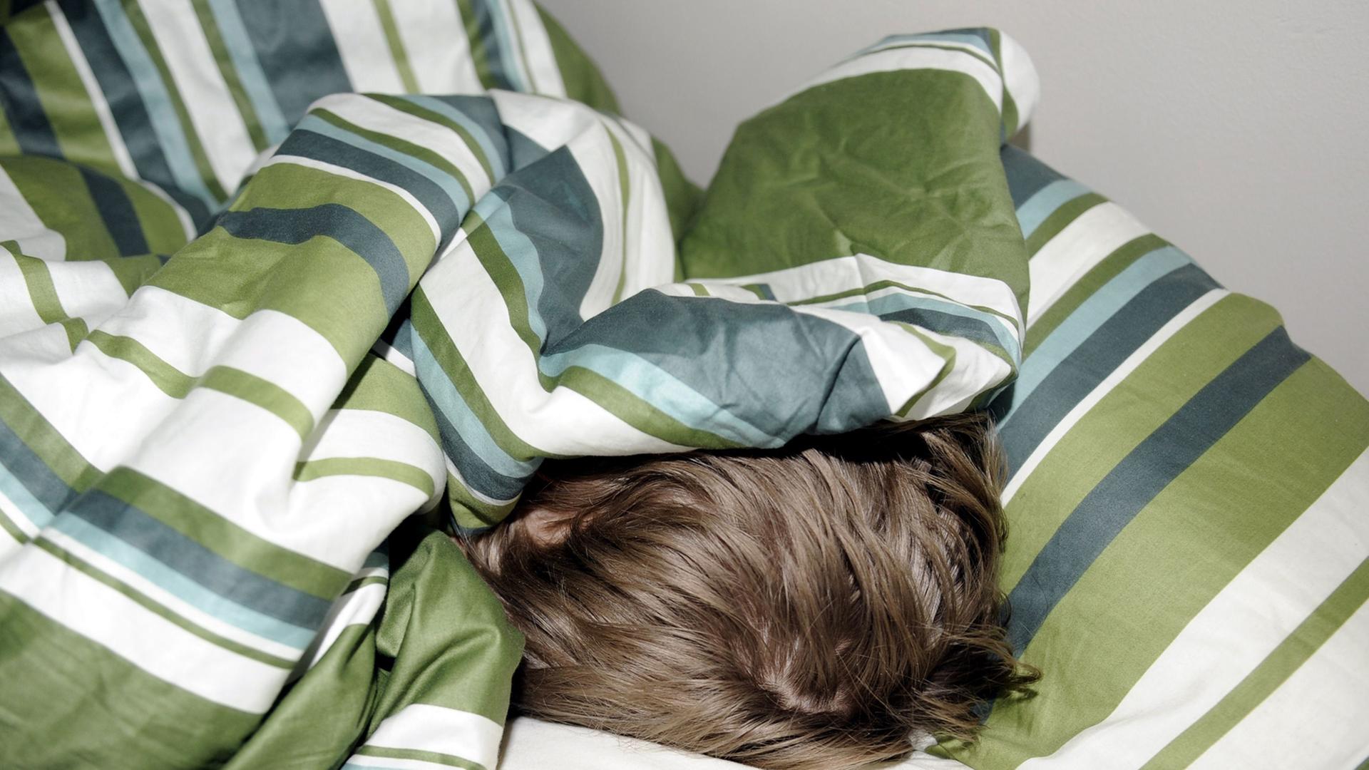 Ein Junge schläft versteckt unter einer gestreiften Bettdecke, nur sein Haarschopf ist zu sehen.