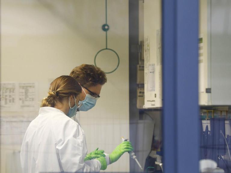 Blick durch ein Fenster der Firma Biontech. Zu sehen sind zwei Mitarbeiterinnen im Labor.
